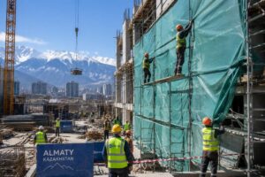 Busy construction site in Almaty with workers installing tarpaulin scaffold protection